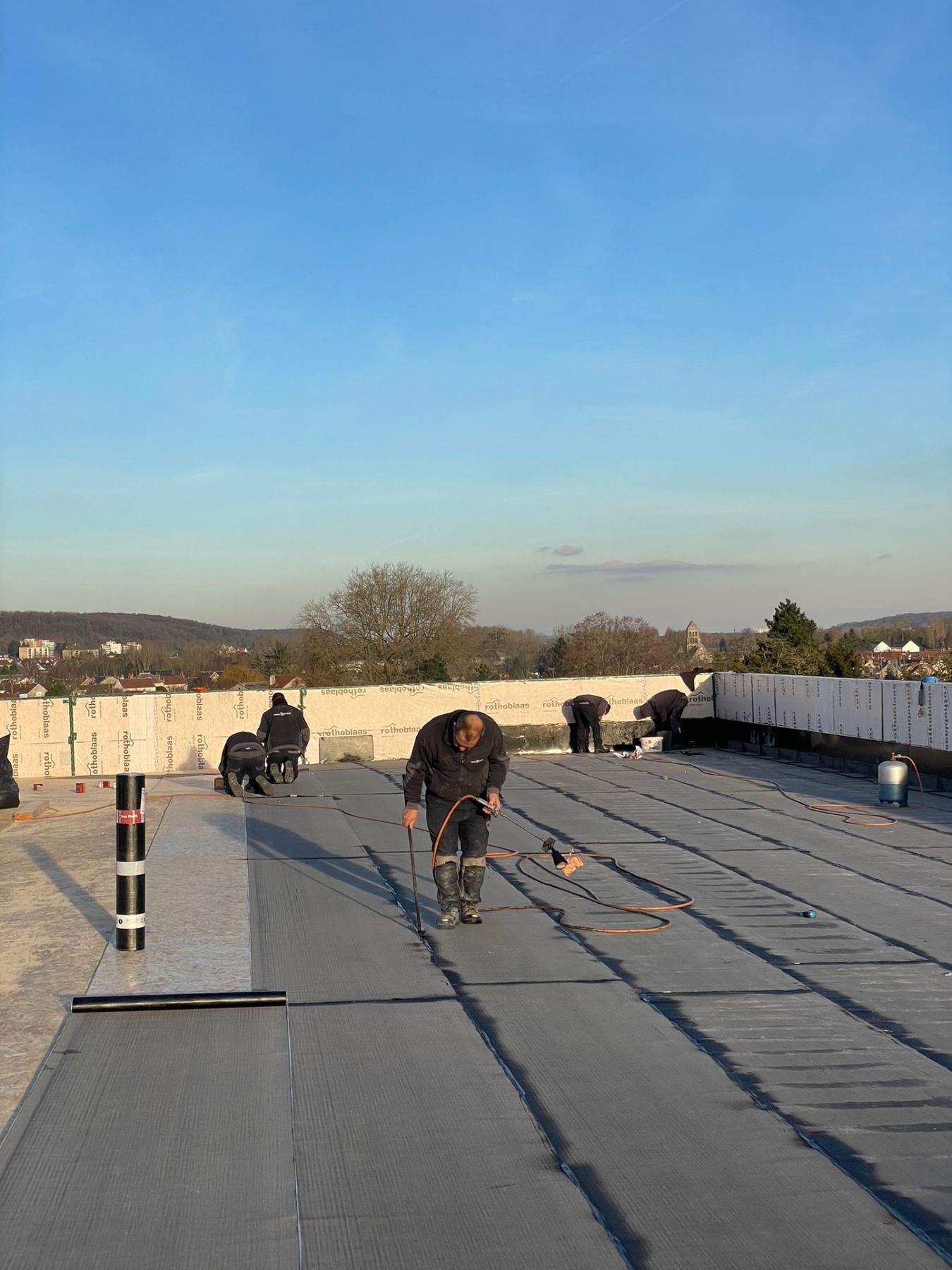 Pose de l'étanchéité bitume par passes successives sur toiture-terrasse, soudure d'un lé au chalumeau
