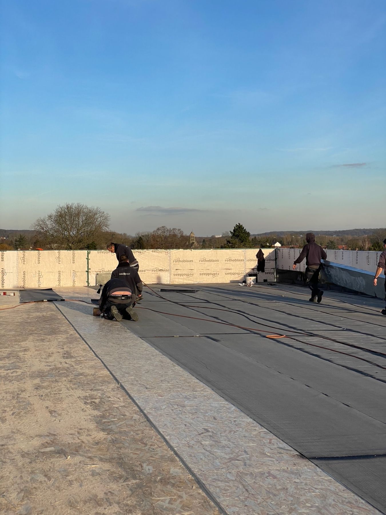 Pose de l'étanchéité bitume par passes successives sur toiture-terrasse, équipe en cours de soudure